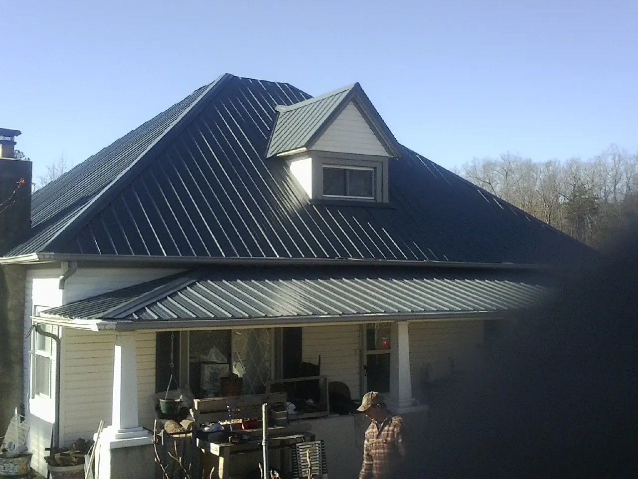 Dark blue standing seam metal roof with a dormer above a front porch in Boyers