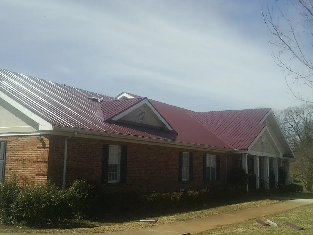 Red metal roof with gabled entries on a long brick building, from a Hail Damage Roof Repair job in Boyers