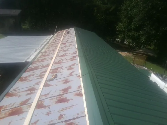 Old rusted panels beside newly installed green metal roofing — Wind Damage Roof Repair by Roofing Brothers in Boyers