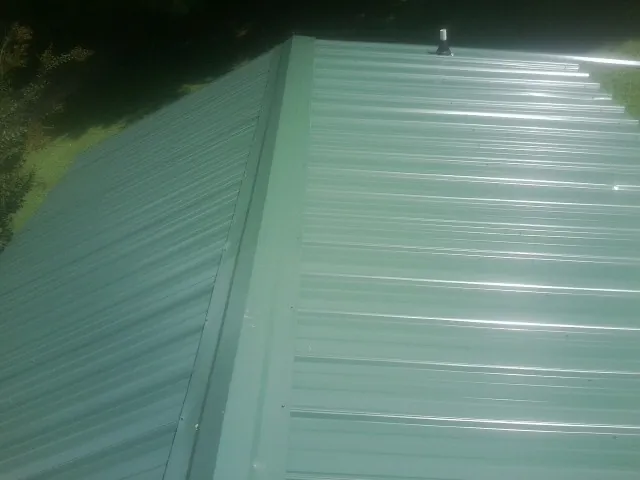 New green metal panels meeting at the ridge of a roof — Flat Roof Repair work by our crew in Boyers