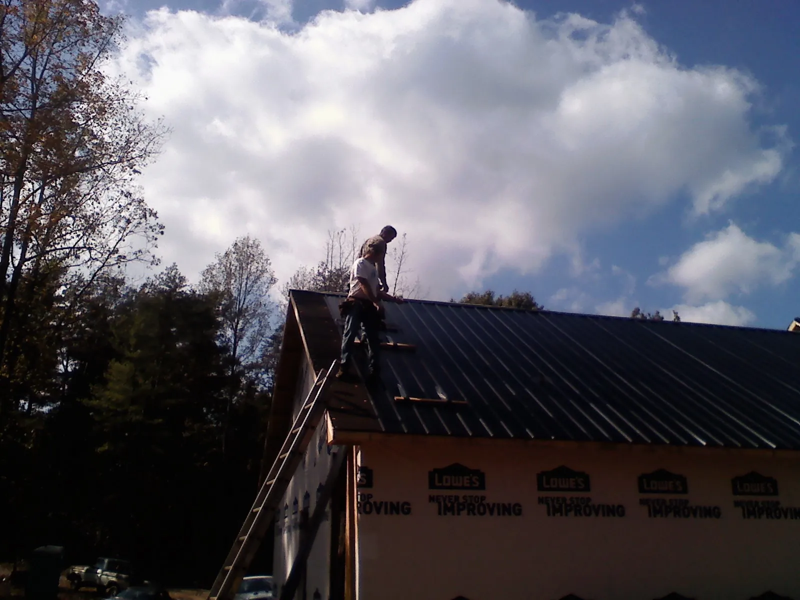 Roofer fastening dark metal panels high against a cloudy sky, from a Roof Inspection job in Boyers