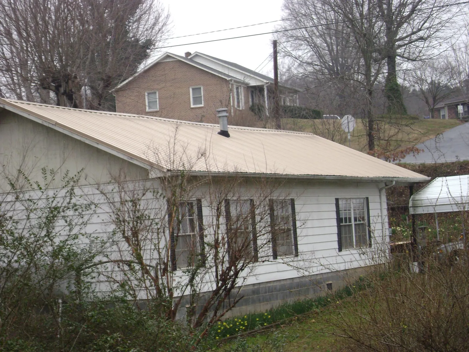 Tan metal roof on a white sided house set into a hillside — Commercial Roofing by Roofing Brothers in Boyers